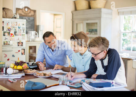 Mid adult man helping adolescents à faire leurs devoirs à la table Banque D'Images