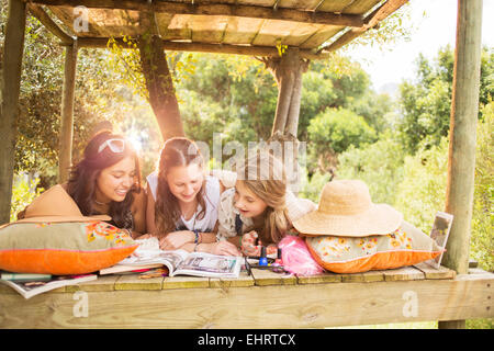 Trois adolescentes reading magazine tout en se trouvant dans la maison de l'arbre en été Banque D'Images