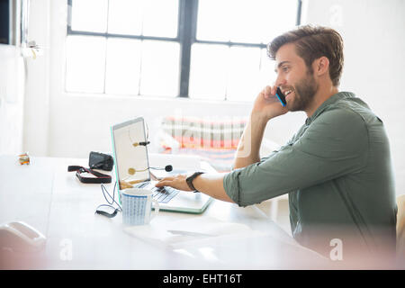 Portrait de jeune homme assis à un bureau avec téléphone mobile et ordinateur portable Banque D'Images