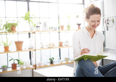 Femme assise sur le comptoir de la cuisine et de l'écriture dans son ordinateur portable Banque D'Images