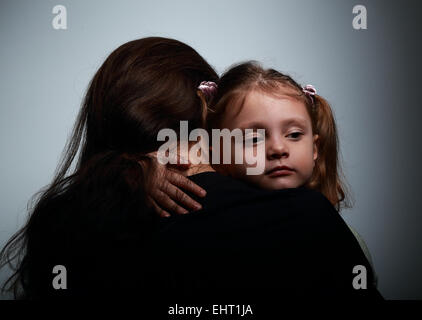 Triste petite fille étreindre sa mère avec amour sur fond sombre Banque D'Images