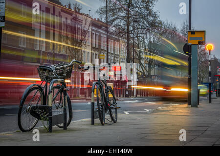 Le trafic passe un couple de enchaîné des vélos sur Caledonian Road à Islington, au nord de Londres, Angleterre. Banque D'Images