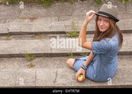 Une jolie jeune fille assise sur les marches dans le parc de la ville. Banque D'Images