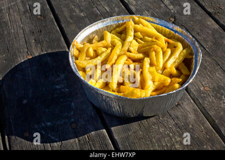 Les frites dans du papier aluminium bac. a servi plus vieille table de pique-nique en bois Banque D'Images