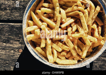 Les frites dans du papier aluminium bac. a servi plus vieille table de pique-nique en bois Banque D'Images