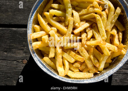 Les frites dans du papier aluminium bac. a servi plus vieille table de pique-nique en bois Banque D'Images