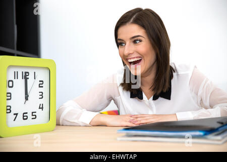 Surpris businesswoman assis à la table et à la recherche sur l'horloge Banque D'Images