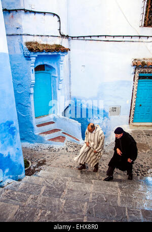 Les deux hommes en djellaba traditionnelle marche sur le bleu à la chaux rue de Chefchaouen, Maroc Banque D'Images