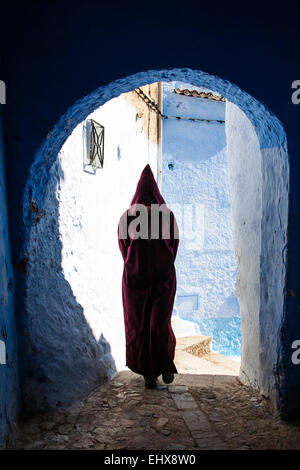 Une femme en djellaba traditionnelle balade le bleu à la chaux rues de Chefchaouen, Maroc Banque D'Images