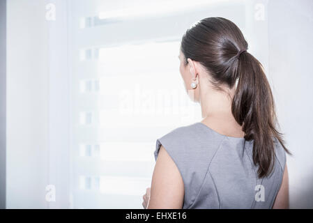 Vue arrière d'une businesswoman looking out office window, Munich, Bavière, Allemagne Banque D'Images