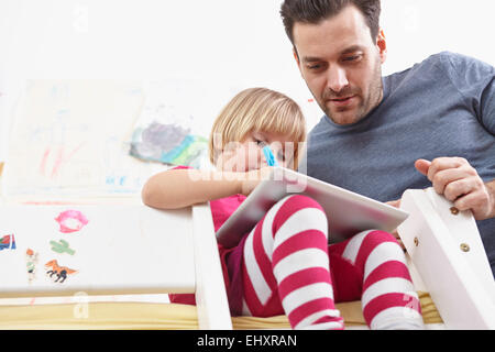 Petite fille assise sur un lit superposé, dessin sur touchpad, père de regarder Banque D'Images