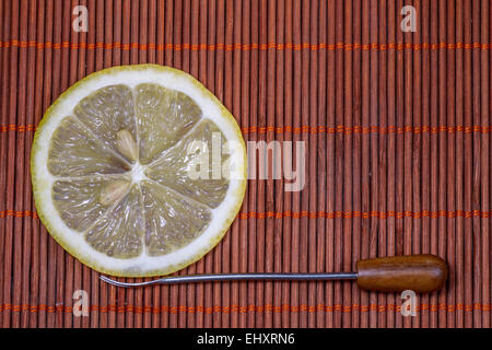 Citron frais tranchés avec la fourche sur un joli tapis en osier comme arrière-plan Banque D'Images