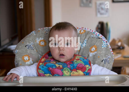 8 mois bébé fille assise dans une chaise haute Banque D'Images