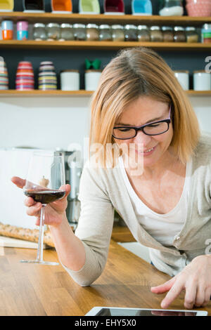 Senior woman holding glass of red wine and using digital tablet Banque D'Images