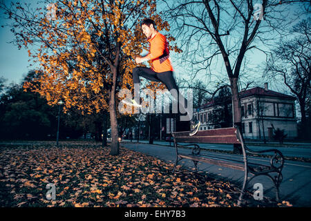 Coureur mâle saute au-dessus de banc dans park