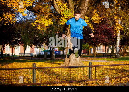 Homme runner jumping over fence in autumn park