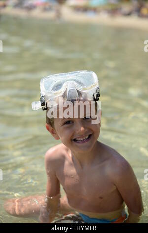 Portrait of a smiling boy sitting dans la mer portant ces lunettes sur sa tête Banque D'Images