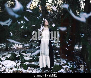 Jeune femme debout dans la forêt avec des plumes tomber tout autour de Banque D'Images