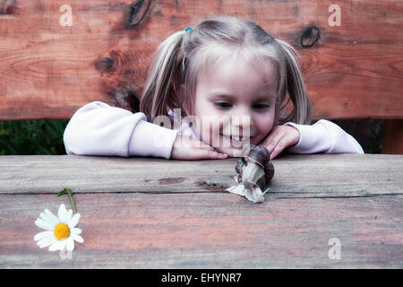 Fille souriante regardant un escargot sur une table en bois dans un jardin, Pologne Banque D'Images