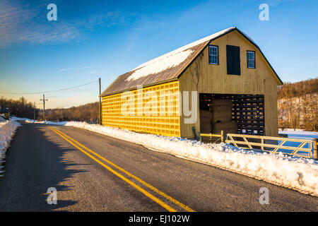 Grange jaune et un champ couvert de neige le long d'une route de campagne dans le comté de York, Pennsylvanie. Banque D'Images