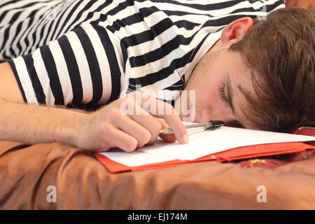 Étudiant fatigué se reposant dans le lit de sa chambre alors qu'il travaillait Banque D'Images