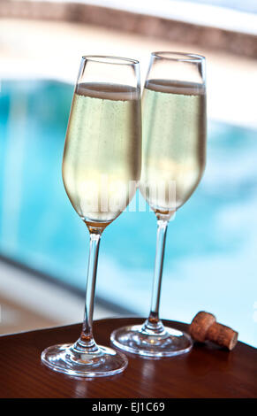 CHAMPAGNE POOL LUXURY fraîchement coulé deux verres de champagne et liège sur table avec terrasse piscine à débordement de luxe en arrière-plan Banque D'Images