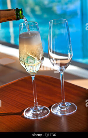 Verseur à VIN MOUSSEUX Fermer voir couler sur les verres réfrigérés de champagne vin sur terrasse ensoleillée avec piscine à débordement de luxe en arrière-plan Banque D'Images