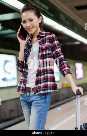 Young woman holding suitcase et au téléphone avec le sourire, Banque D'Images