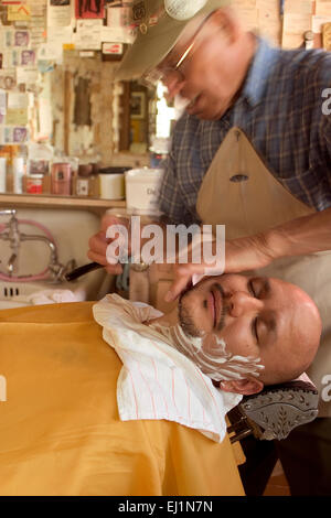 Angel Delgadillo rasage un client à son barbier sur l'historique Route 66 à Seligman, Arizona Banque D'Images