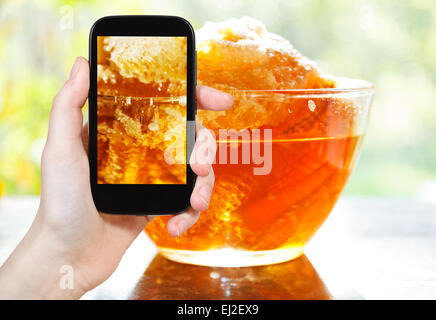 Photographiant food concept - office prend photo de miel frais dans le peigne dans bol en verre à table sur smartphone, Russie Banque D'Images