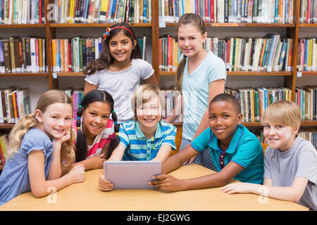 Cute pupils using tablet computer in library Banque D'Images