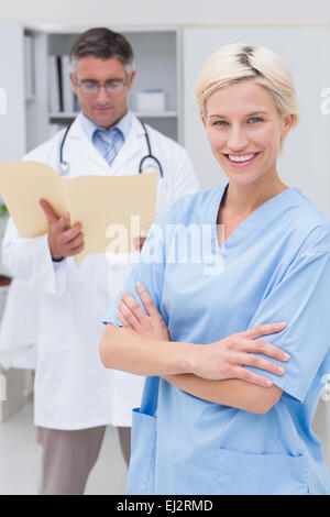 Nurse standing les bras croisés alors que la lecture de rapports médecin en clinique Banque D'Images