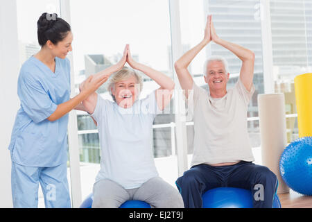 Senior couple on exercice ball étant assisté par le formateur Banque D'Images