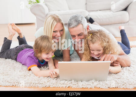 Family using laptop ensemble tout en se trouvant sur un tapis Banque D'Images