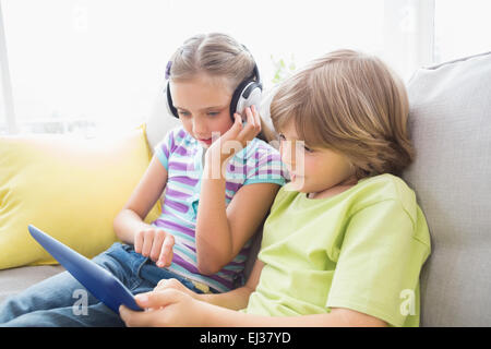 Frères et sœurs à l'aide de tablette numérique tout en écoutant de la musique Banque D'Images