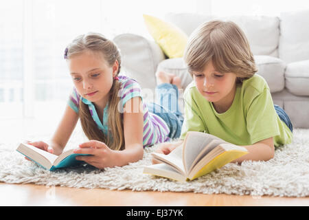 Frères et sœurs lire des livres tout en se trouvant sur un tapis Banque D'Images