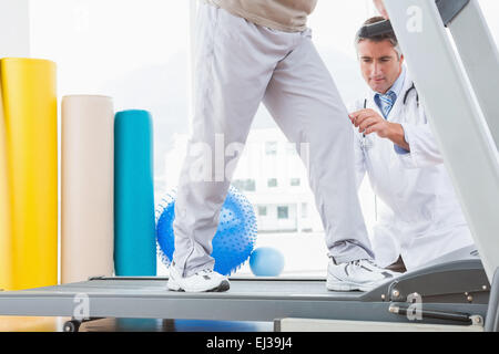 Man sur tapis roulant avec le thérapeute crouching Banque D'Images