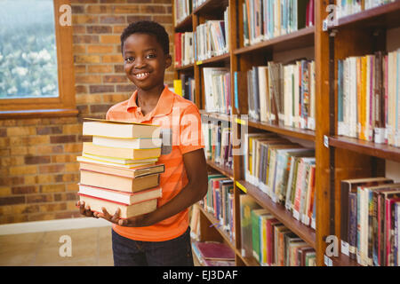 Portrait of cute boy carrying books in library Banque D'Images