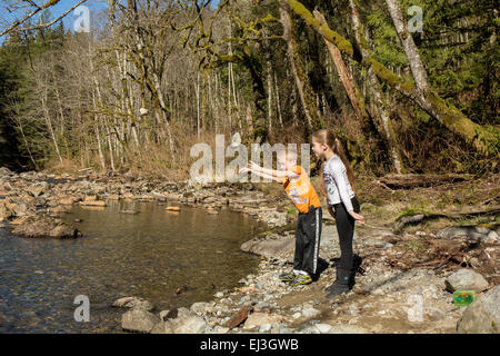 Neuf ans, fille et garçon de sept ans jeter des pierres dans la rivière Snoqualmie près de North Bend, Oregon, USA Banque D'Images