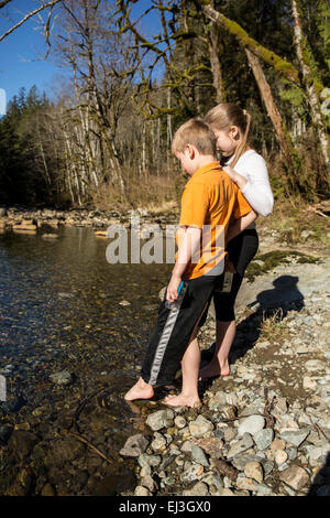 Un garçon de sept ans et sa sœur de neuf ans d'essais avec précaution la froideur de la rivière Snoqualmie, avec leurs orteils Banque D'Images