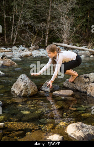 Neuf ans, fille, comme l'équilibrage elle monte sur des rochers dans la rivière peu profonde Snoqualmie, près de North Bend, Oregon, USA Banque D'Images