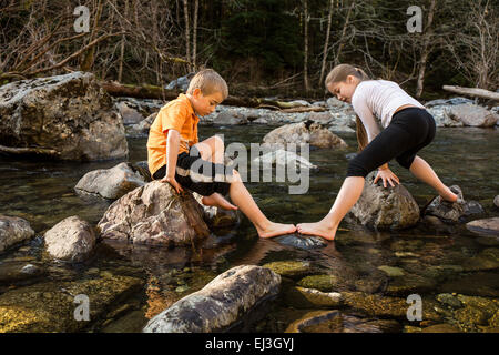 Impasse d'une fillette de 9 ans qui veulent aller dans le sens opposé de son frère de 7 ans que le rock hop dans la rivière Banque D'Images