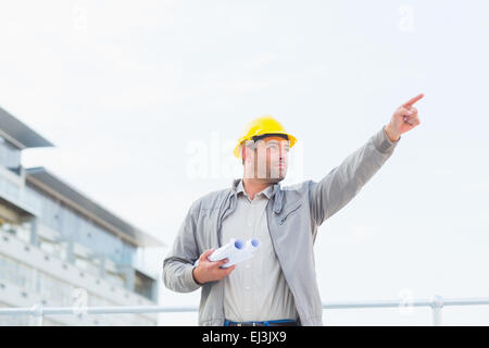 Architect with blueprints pointant vers sky Banque D'Images