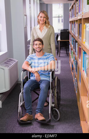 Smiling étudiante handicapée avec camarade in library Banque D'Images