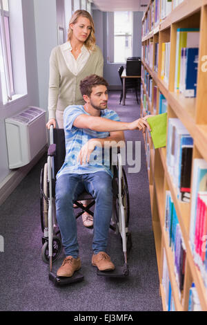 Smiling étudiante handicapée avec camarade in library Banque D'Images