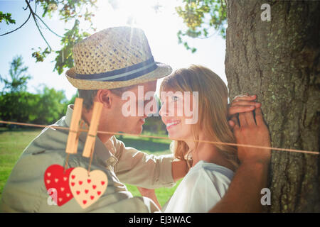 Image composite de cute smiling couple leaning against tree dans le parc Banque D'Images