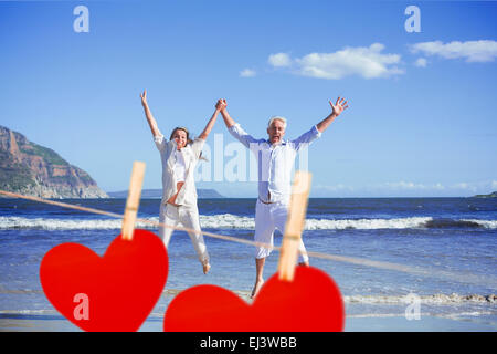 Image composite de l'heureux couple sauter pieds nus sur la plage Banque D'Images