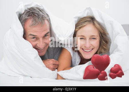 Image composite de l'heureux couple d'âge moyen sous la couette Banque D'Images