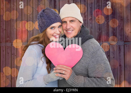 Image composite de l'heureux couple dans des vêtements chauds holding heart Banque D'Images