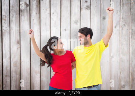 Image composite de l'heureux couple cheering in t-shirts rouge et jaune Banque D'Images
